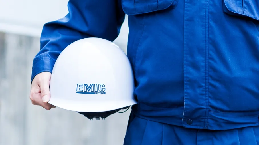 EMICのロゴが入ったヘルメットを手に持つ作業服姿の人物